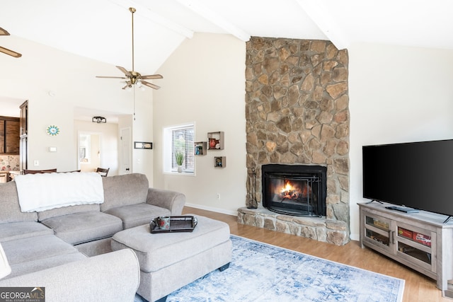 living room with light hardwood / wood-style floors, beamed ceiling, ceiling fan, a stone fireplace, and high vaulted ceiling