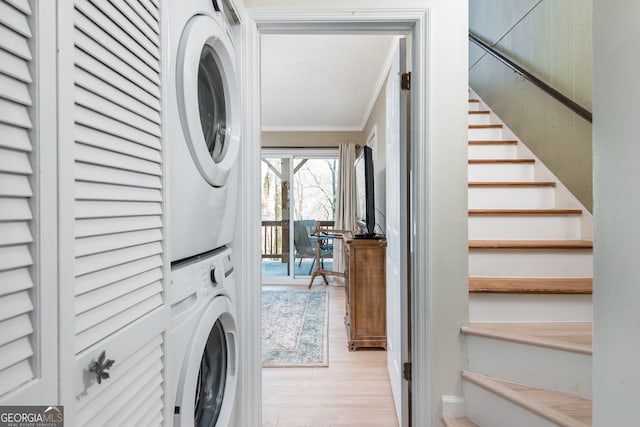 laundry area featuring light hardwood / wood-style flooring, stacked washer and dryer, and ornamental molding