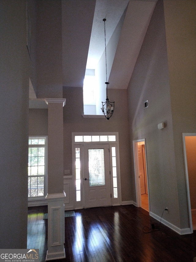 foyer with a towering ceiling, dark hardwood / wood-style floors, decorative columns, and a notable chandelier