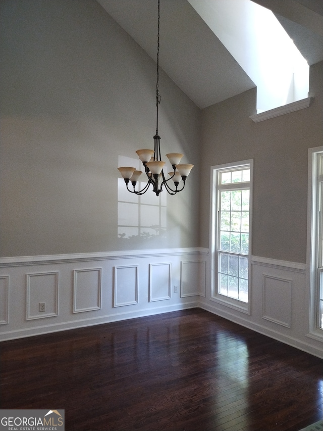 unfurnished dining area with dark wood-type flooring, a notable chandelier, and high vaulted ceiling