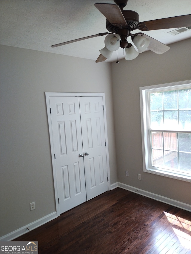 unfurnished bedroom featuring dark wood-type flooring, a closet, ceiling fan, and a textured ceiling