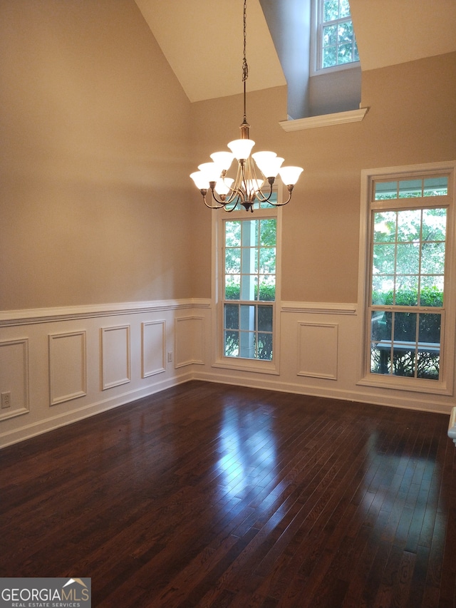 spare room featuring high vaulted ceiling, dark hardwood / wood-style floors, an inviting chandelier, and a healthy amount of sunlight