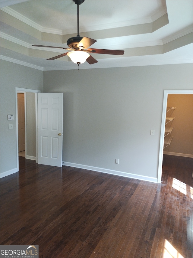 spare room featuring dark wood-type flooring, ceiling fan, ornamental molding, and a tray ceiling