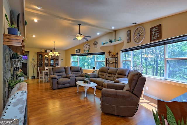 living room featuring high vaulted ceiling, ceiling fan with notable chandelier, a stone fireplace, and wood-type flooring