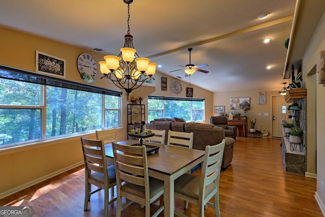 dining space featuring lofted ceiling, a stone fireplace, ceiling fan with notable chandelier, and wood-type flooring