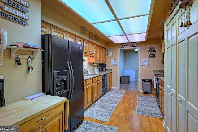 kitchen with black appliances, butcher block countertops, sink, and light hardwood / wood-style floors