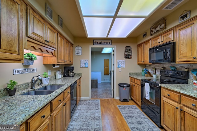 kitchen featuring tasteful backsplash, light hardwood / wood-style flooring, black appliances, sink, and light stone countertops