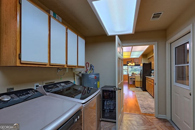 clothes washing area with cabinets, light hardwood / wood-style flooring, a notable chandelier, washer and dryer, and electric water heater