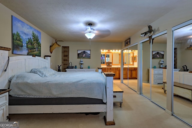 bedroom featuring a textured ceiling, connected bathroom, ceiling fan, two closets, and carpet floors