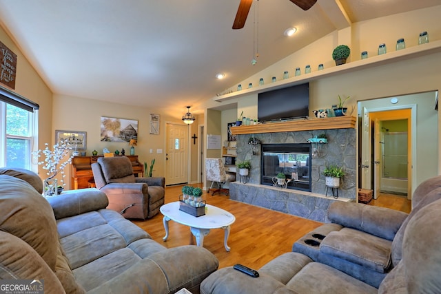 living room with vaulted ceiling, hardwood / wood-style flooring, ceiling fan, and a stone fireplace