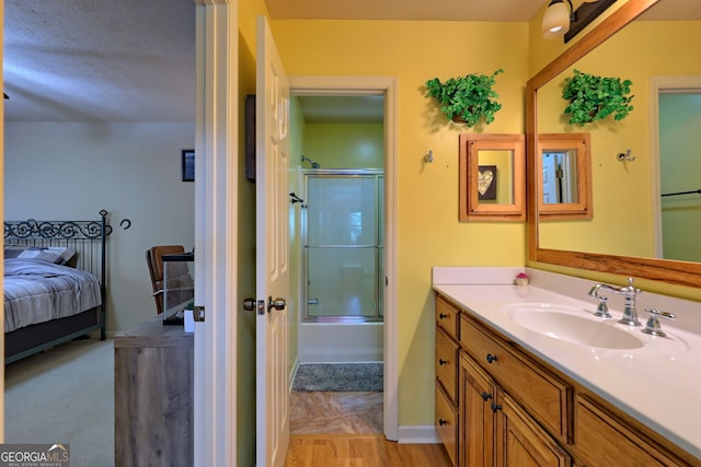 bathroom with combined bath / shower with glass door, vanity, and a textured ceiling