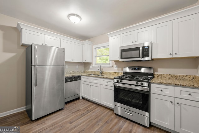 kitchen with light stone counters, stainless steel appliances, light hardwood / wood-style floors, and white cabinetry