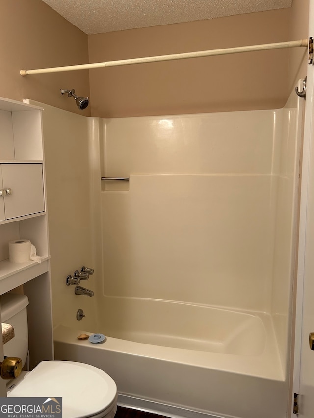 bathroom featuring toilet, bathing tub / shower combination, and a textured ceiling