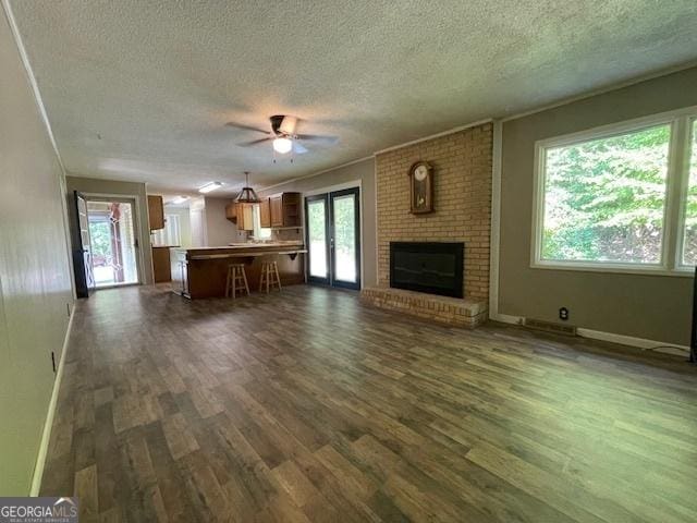 unfurnished living room featuring ceiling fan, dark hardwood / wood-style floors, a textured ceiling, a brick fireplace, and french doors