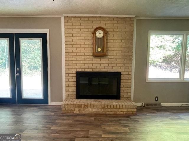 unfurnished living room featuring french doors, crown molding, a brick fireplace, a textured ceiling, and dark hardwood / wood-style floors