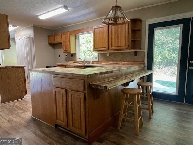 kitchen with hanging light fixtures, crown molding, dark wood-type flooring, and a kitchen breakfast bar