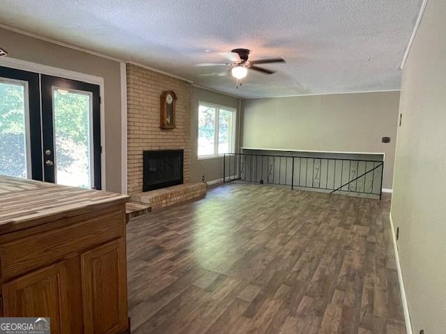 unfurnished living room with french doors, a brick fireplace, a textured ceiling, dark hardwood / wood-style flooring, and ceiling fan