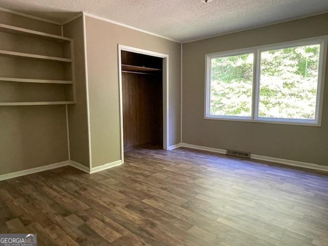 unfurnished bedroom with dark wood-type flooring, ornamental molding, a closet, and a textured ceiling