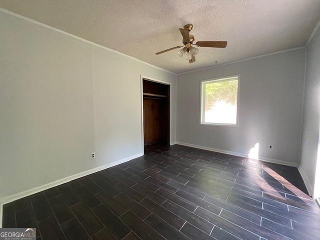 unfurnished bedroom featuring ceiling fan, dark hardwood / wood-style floors, ornamental molding, a textured ceiling, and a closet