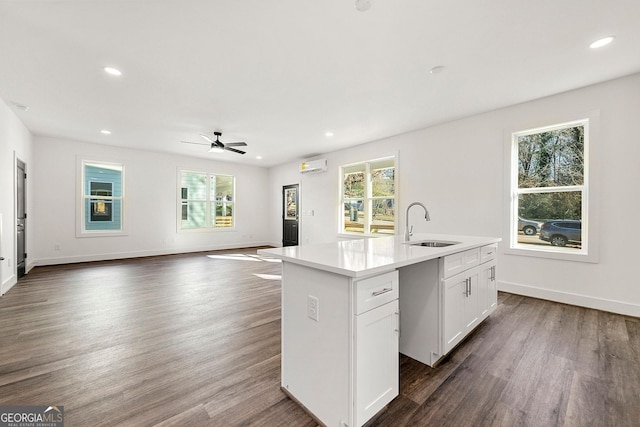 kitchen featuring a wall mounted air conditioner, a kitchen island with sink, white cabinets, sink, and ceiling fan