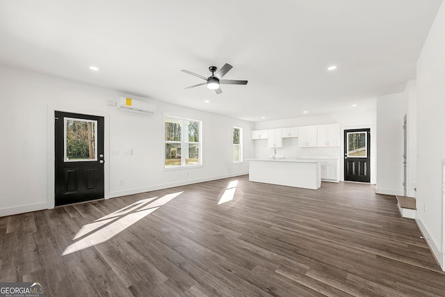 unfurnished living room with an AC wall unit, ceiling fan, sink, and dark wood-type flooring