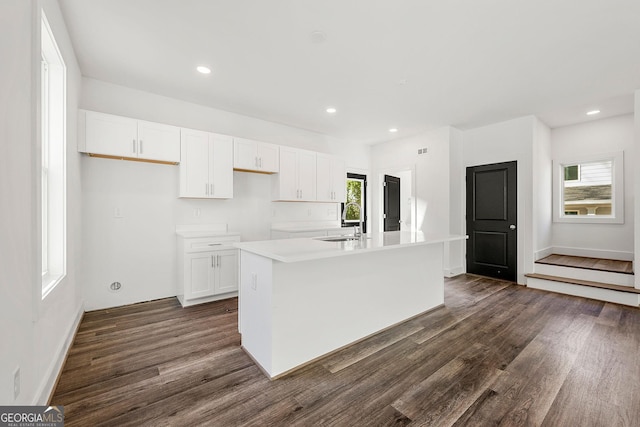 kitchen with dark hardwood / wood-style flooring, white cabinetry, a center island with sink, and sink