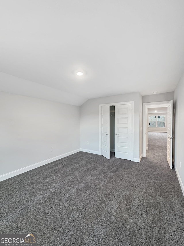 unfurnished bedroom with dark colored carpet, a closet, and lofted ceiling