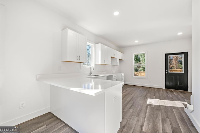 kitchen with kitchen peninsula, white cabinetry, sink, and light hardwood / wood-style flooring