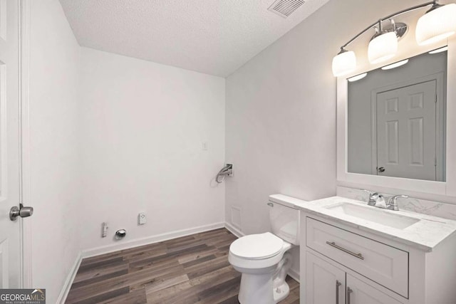 bathroom with wood-type flooring, toilet, vanity, and a textured ceiling