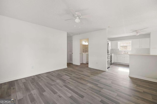 unfurnished living room with a textured ceiling, ceiling fan, dark hardwood / wood-style floors, and sink