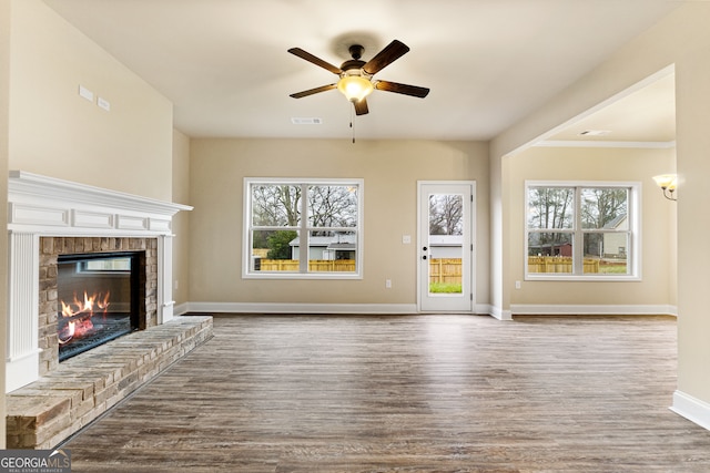 unfurnished living room featuring plenty of natural light, a brick fireplace, wood-type flooring, and ceiling fan