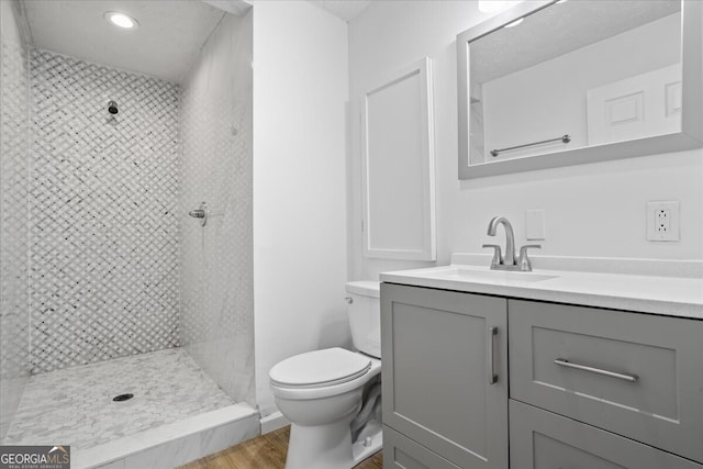 bathroom featuring vanity, toilet, a tile shower, and hardwood / wood-style floors