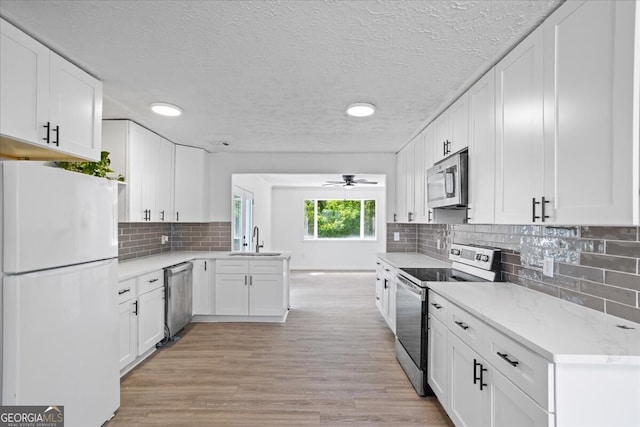 kitchen with appliances with stainless steel finishes, light hardwood / wood-style floors, sink, white cabinetry, and ceiling fan