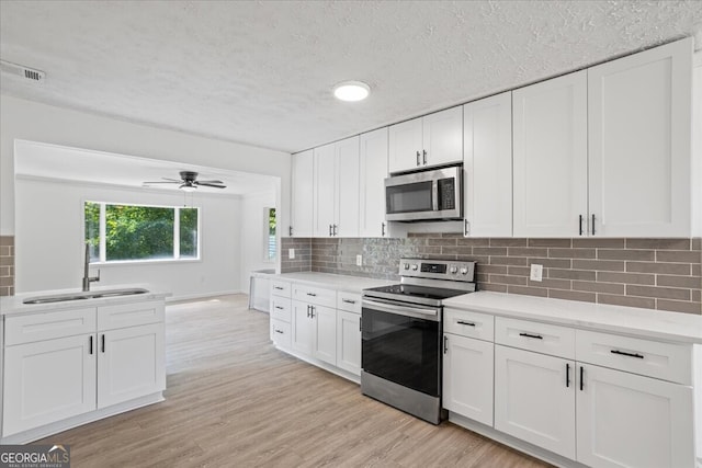 kitchen with appliances with stainless steel finishes, light hardwood / wood-style floors, white cabinetry, ceiling fan, and tasteful backsplash