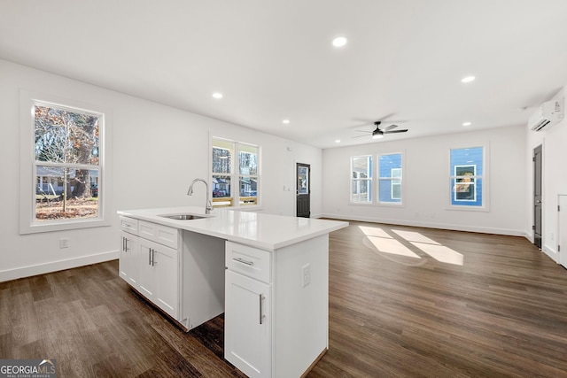 kitchen featuring a wall mounted air conditioner, a kitchen island with sink, sink, ceiling fan, and white cabinetry