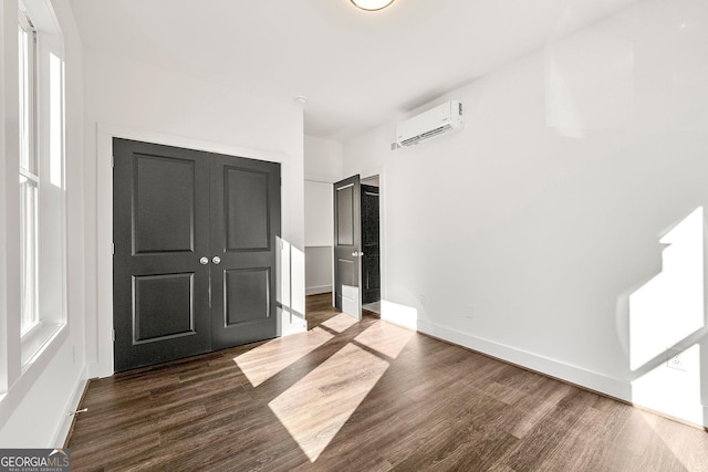 unfurnished bedroom featuring dark hardwood / wood-style flooring, a closet, multiple windows, and a wall mounted air conditioner