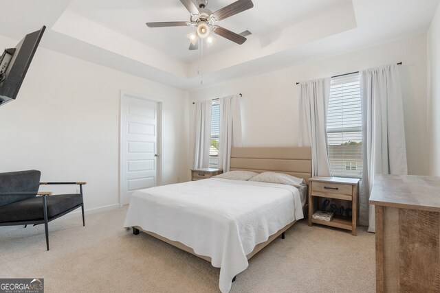 bedroom with light colored carpet, ceiling fan, and a tray ceiling