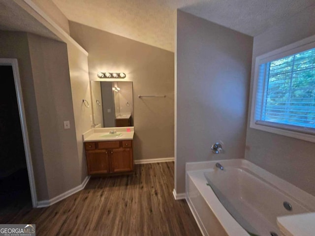 bathroom with a textured ceiling, vanity, wood-type flooring, lofted ceiling, and a washtub