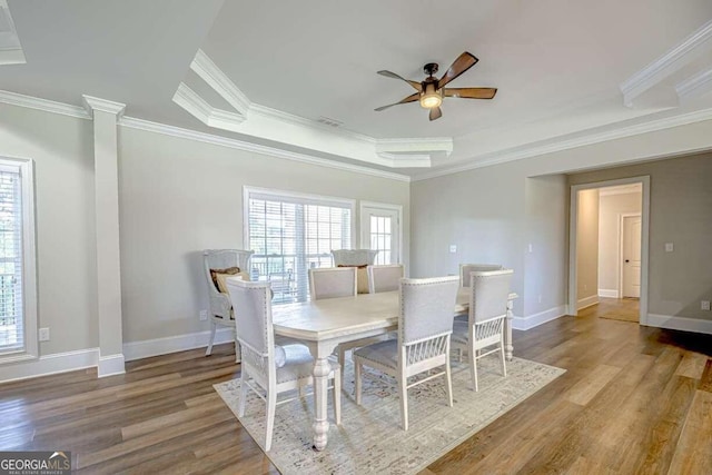 dining area with crown molding, ceiling fan, a raised ceiling, hardwood / wood-style flooring, and ornate columns