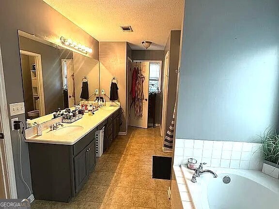 bathroom featuring a relaxing tiled tub, a textured ceiling, and vanity