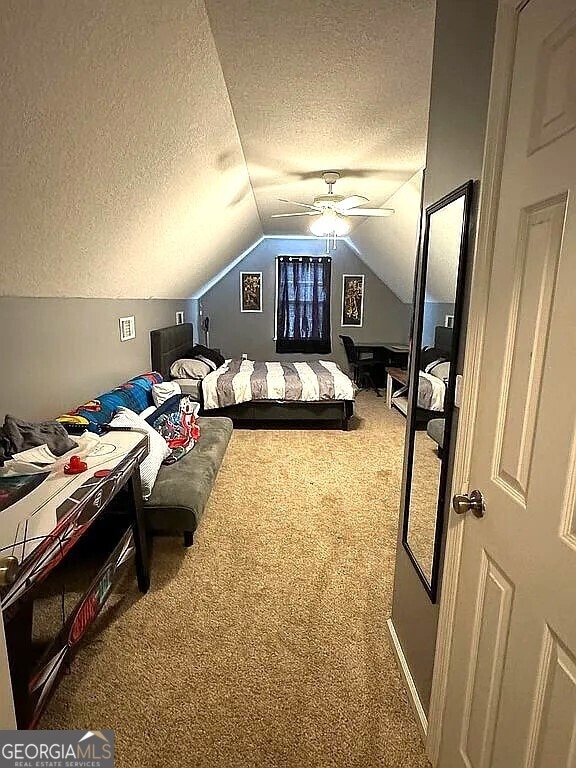 carpeted bedroom featuring ceiling fan, vaulted ceiling, and a textured ceiling