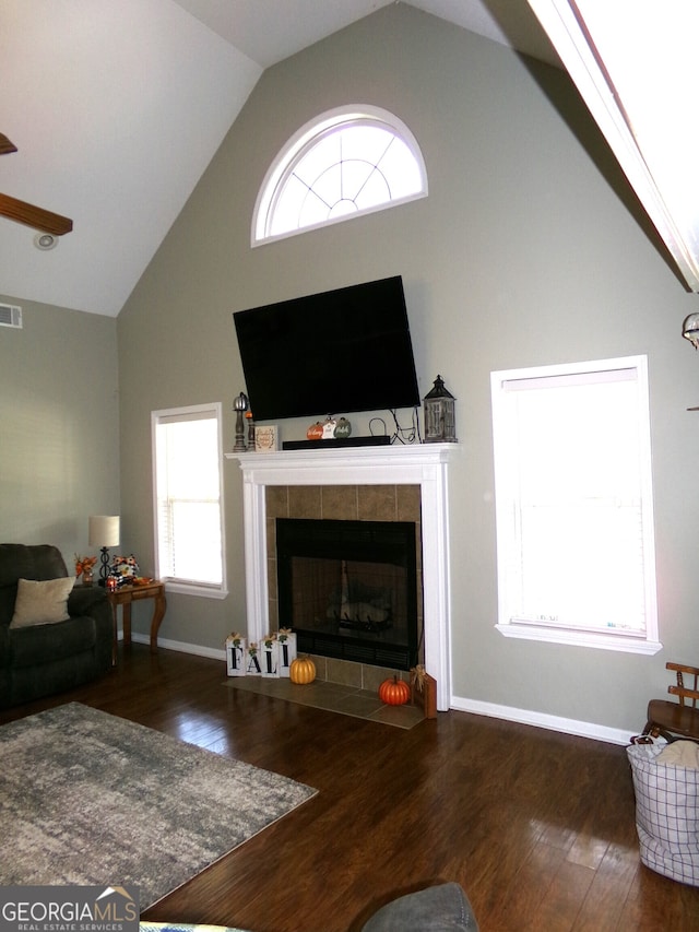 living room featuring dark hardwood / wood-style flooring, high vaulted ceiling, ceiling fan, and a tile fireplace