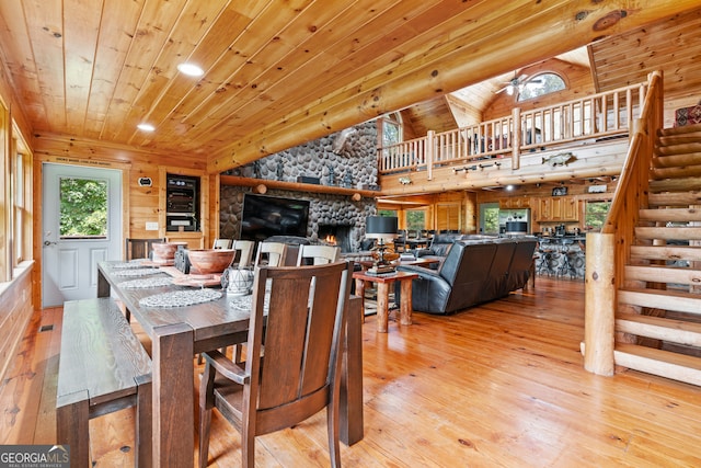 dining room with a fireplace, wooden walls, vaulted ceiling, light wood-type flooring, and wood ceiling