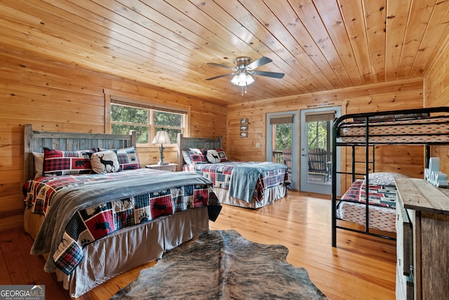 bedroom with access to exterior, ceiling fan, wood walls, and light hardwood / wood-style floors