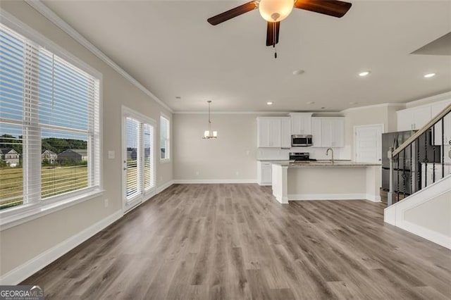 unfurnished living room with crown molding, sink, ceiling fan with notable chandelier, and hardwood / wood-style flooring