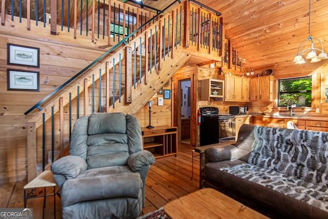 living room featuring high vaulted ceiling, an inviting chandelier, wooden walls, and light hardwood / wood-style floors