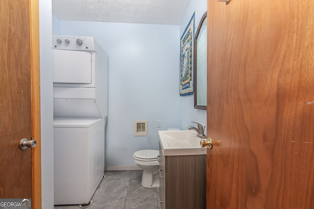 bathroom featuring tile patterned flooring, toilet, stacked washing maching and dryer, vanity, and a textured ceiling