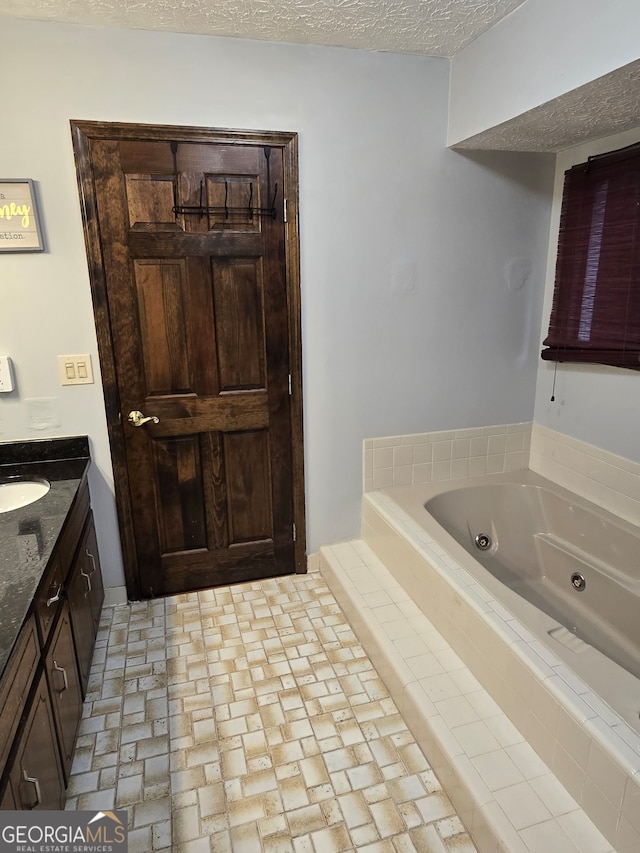 bathroom with tiled tub, vanity, and a textured ceiling