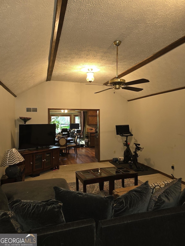 living room with a textured ceiling, ceiling fan, visible vents, vaulted ceiling with beams, and wood finished floors