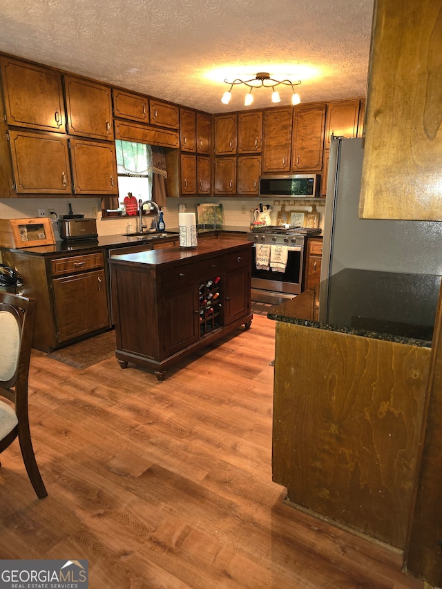 kitchen with light hardwood / wood-style floors, a textured ceiling, a center island, rail lighting, and appliances with stainless steel finishes